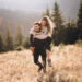 Stylish model couple in the autumn mountains. A young guy and a girl run along the slope against the background of the forest and mountain peaks at sunset.