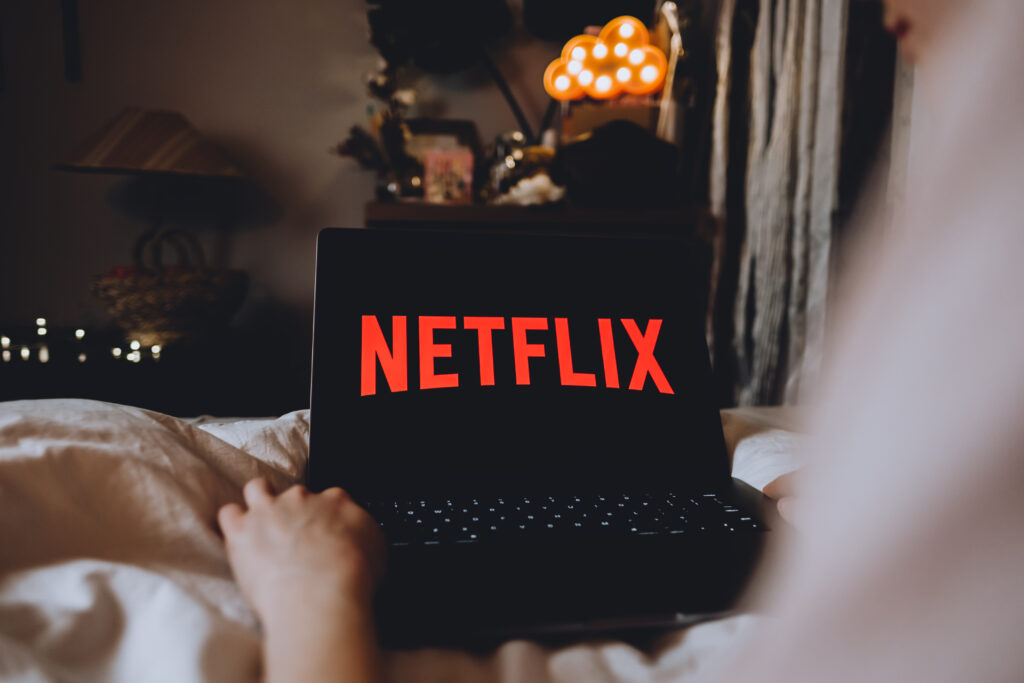 Netflix logo on the laptop screen. Young woman watching netflix channel sitting at home in the evening.